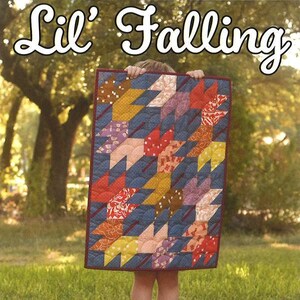 May include: A child holds up a colorful quilt with a geometric pattern. The quilt is titled "Lil' Falling" and is a Running Doe Quilts exclusive mini quilt.