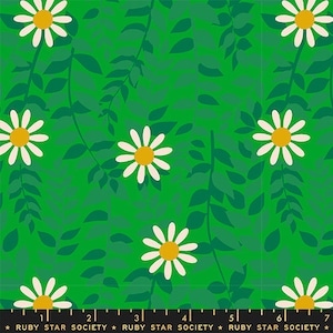 May include: A green fabric with a repeating pattern of white daisies and dark green leaves. The fabric has a white and gold ruler with numbers printed on it.