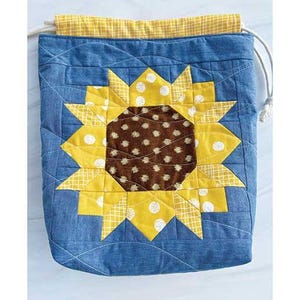 May include: A blue drawstring bag with a sunflower design. The sunflower is made of yellow fabric with white polka dots and a brown center. The bag is 11 inches wide, 10 inches tall, and 4 inches deep. "Mini Sunflower Drawstring Bag Project" and "by Chrissy Lux of Branch & Blume" are written below the bag.