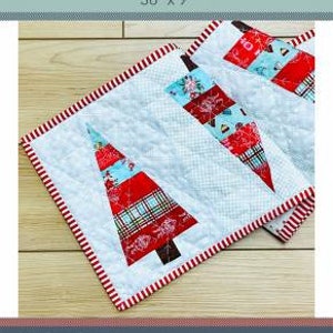May include: A white table runner with a red and blue striped border and a pattern of three stylized Christmas trees. The trees are made of red, blue, and white fabric with a plaid pattern. The runner is 36 inches by 9 inches.