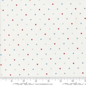 May include: White fabric with a repeating pattern of red, blue, and gray polka dots. The dots are evenly spaced across the surface. A ruler is visible along the bottom edge.