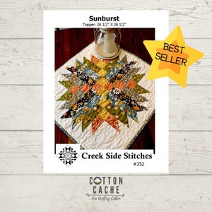May include: A quilt pattern for a Sunburst table topper, measuring 26 1/2 inches by 26 1/2 inches. The pattern features a starburst design with a variety of floral fabrics in shades of orange, yellow, green, and blue. The pattern is labeled "Creek Side Stitches #352" and is a best seller.