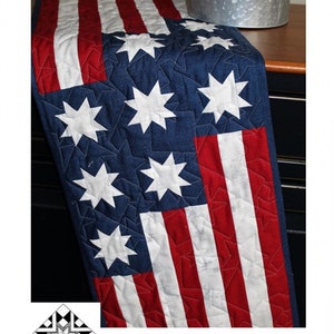 May include: A red, white, and blue quilted table runner with a star pattern. The runner is 13 1/2 inches by 41 1/2 inches. The text "Stars & Stripes" and "Creek Side Stitches #378" is visible.