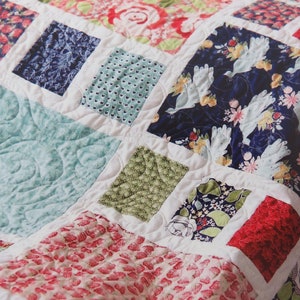 May include: A patchwork quilt with a variety of floral and geometric patterns in shades of red, blue, green, and white. The quilt is made of squares and rectangles, and the seams are visible.
