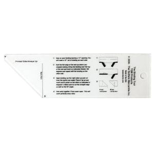May include: White plastic tool with instructions for sewing binding on fabric. The tool has a 45-degree angle and a 12-inch opening. The text on the tool reads "The Binding Tool" and "TOM Products - The Quilters Mercantile Inc."
