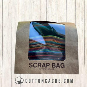 May include: A brown paper bag with a clear window displaying colorful fabric scraps. The bag is labeled "SCRAP BAG" with a net weight of approximately 1/2 lb. The website "cottoncache.com" is printed at the bottom.
