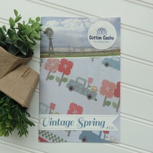 May include: A white fabric with a blue truck, pink flowers, and a windmill on a blue sky background. The fabric is labeled "Vintage Spring #110" and "Cotton Cache Fine Quilting Cotton".