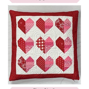 May include: A square pillow with a red border and a white center featuring nine patchwork hearts in shades of red and pink. The pillow measures 18 inches by 18 inches and is labeled "Heartstrings Pillow."