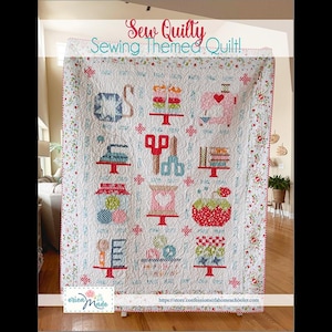 May include: A white quilt with sewing-themed designs, including scissors, spools, and cakes. The quilt has a floral border and the text "Sew Quilty Sewing Themed Quilt!" in pink and teal. The quilt is displayed indoors.