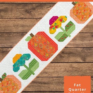 May include: A white table runner with a repeating pattern of colorful pumpkins and flowers. The runner is 19 inches by 69 inches. The text "Pumpkins and Petals Table Runner" is displayed at the top.