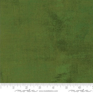 May include: A solid green fabric with a subtle textured pattern. The fabric is a medium green color with a slightly darker green hue in some areas. The fabric is shown with a ruler that reads "moda" and "www.modafabrics.com".