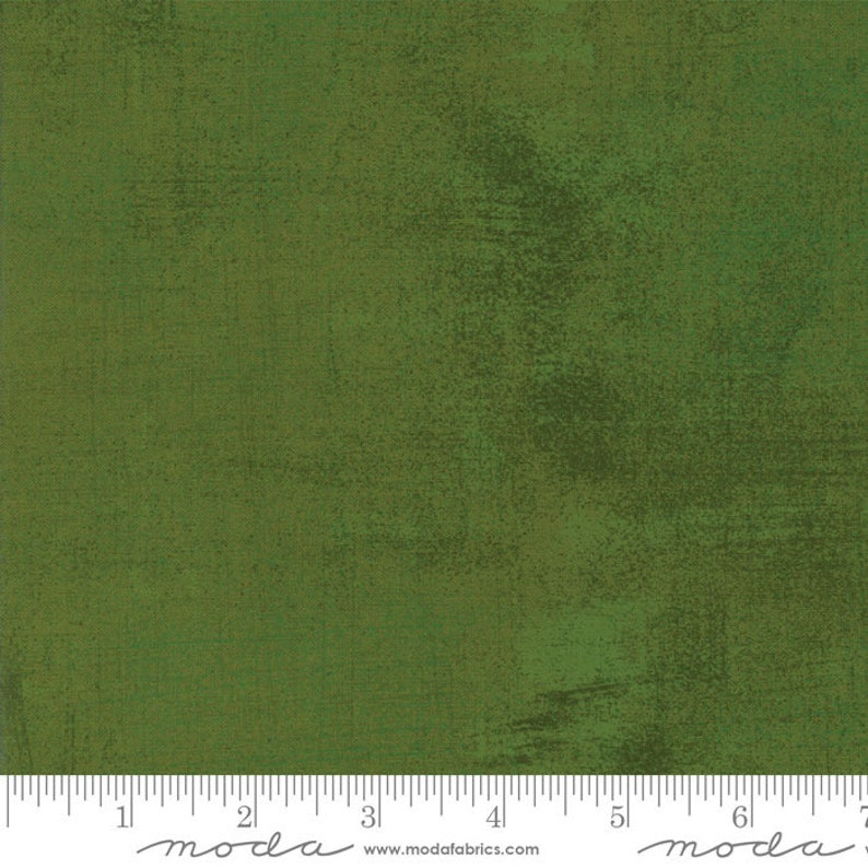 May include: A solid green fabric with a subtle textured pattern. The fabric is a medium green color with a slightly darker green hue in some areas. The fabric is shown with a ruler that reads "moda" and "www.modafabrics.com".