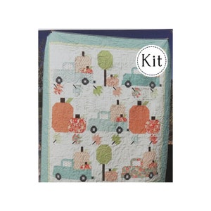 May include: A quilt kit featuring a patchwork design of blue trucks carrying pumpkins and fall leaves. The quilt is made with a white background and features a variety of colors, including orange, green, and brown. The text "Kit" is written in a circle on the quilt.
