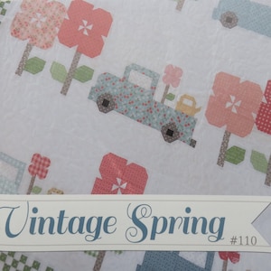 May include: Vintage Spring quilt pattern featuring a blue truck carrying a flower and a watering can, with pink and white flowers and green leaves. The pattern is labeled "Vintage Spring #110".