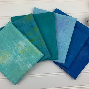 May include: A set of six fabric squares in shades of blue and green. The fabric has a textured, slightly distressed look.
