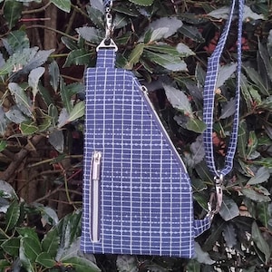 May include: A blue and white patterned fabric sling bag with a zipper closure and a silver chain strap. The bag measures 6 inches wide by 10 inches high by 1 1/2 inches deep. The bag is hanging from a branch in a bush.