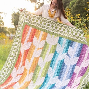 May include: A colorful quilt with a rainbow striped design and white tulip-shaped patterns. The quilt has a green border with a white floral pattern. The text "Field of Joy" is at the top.