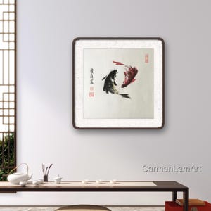 May include: A framed artwork featuring two koi fish in a traditional Asian style. One fish is black, the other is red, and they are depicted swimming in opposite directions. The artwork is set against a white background with calligraphy and red stamps.