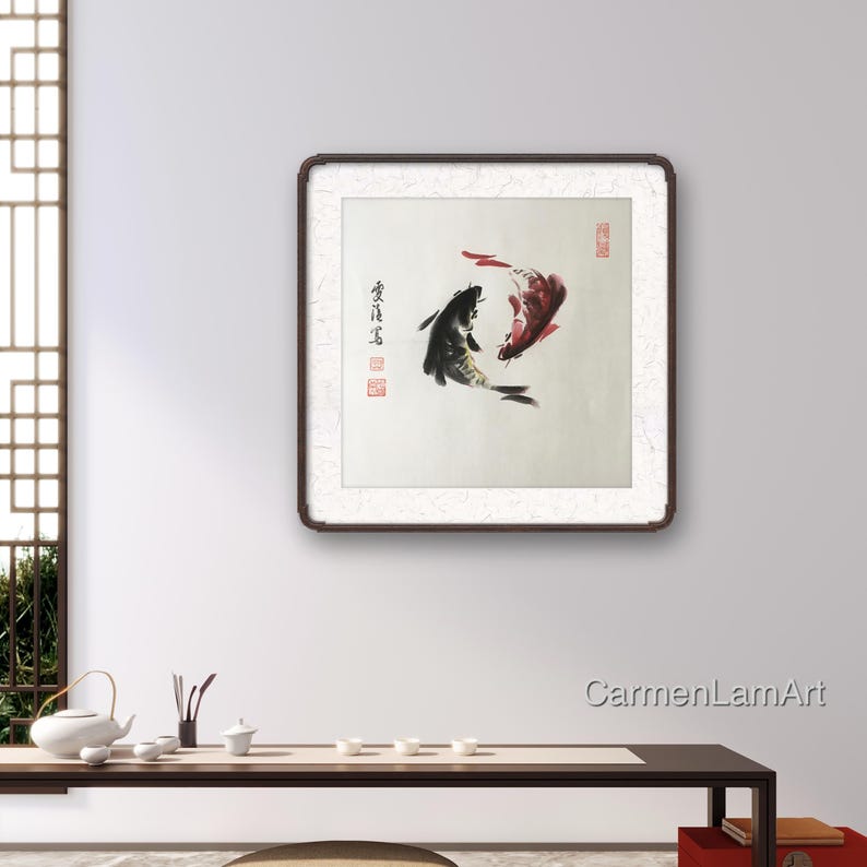 May include: A framed artwork featuring two koi fish in a traditional Asian style. One fish is black, the other is red, and they are depicted swimming in opposite directions. The artwork is set against a white background with calligraphy and red stamps.