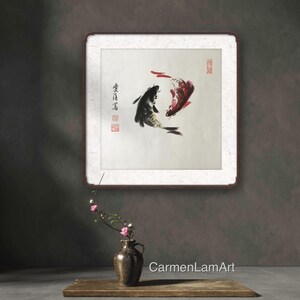 May include: An Asian-inspired artwork featuring two koi fish in shades of black and red, painted on a white background. The artwork is framed in a dark brown frame and includes Chinese characters and red stamps. A vase with flowers sits in front of the artwork.