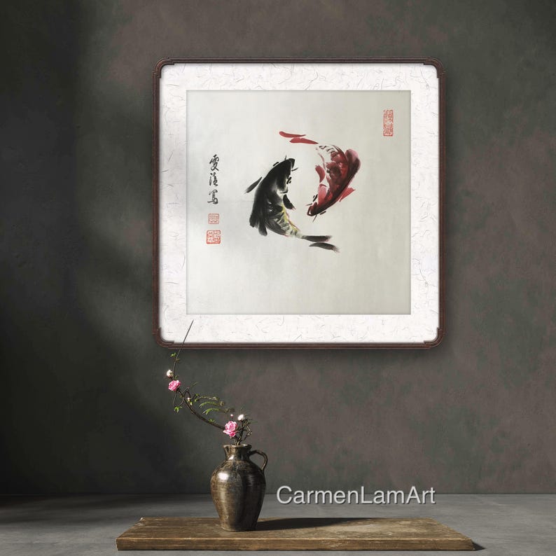 May include: An Asian-inspired artwork featuring two koi fish in shades of black and red, painted on a white background. The artwork is framed in a dark brown frame and includes Chinese characters and red stamps. A vase with flowers sits in front of the artwork.