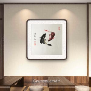 May include: Framed artwork featuring two koi fish in a traditional Asian ink painting style. One fish is black, the other red, swimming in opposite directions. The artwork is displayed on a neutral-toned wall.
