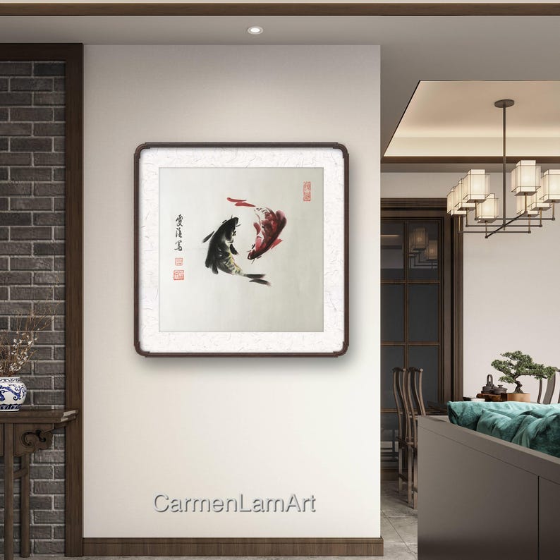 May include: A framed artwork featuring two koi fish in a traditional Asian ink painting style. One fish is black, the other red, with brushstrokes and calligraphy. The artwork is displayed on a white wall.