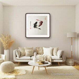 May include: A framed artwork depicts two koi fish in a traditional Asian ink painting style. One fish is black, the other red, with calligraphy and red stamps. The artwork hangs above a white sofa in a living room.