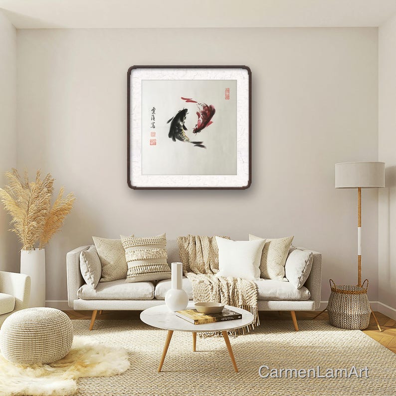 May include: A framed artwork depicts two koi fish in a traditional Asian ink painting style. One fish is black, the other red, with calligraphy and red stamps. The artwork hangs above a white sofa in a living room.