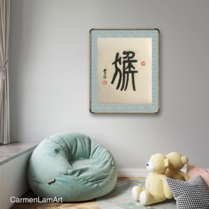 Puede incluir: Una obra de arte de caligraf&iacute;a enmarcada con el car&aacute;cter chino "解" (jie) en tinta negra sobre un fondo beige. El marco es azul claro con un borde de madera. La obra est&aacute; colgada en una pared gris claro.