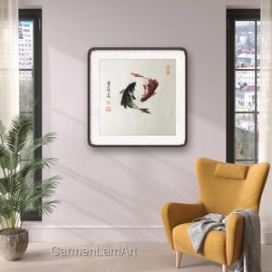 May include: A framed artwork featuring two koi fish in a traditional Asian ink painting style. One fish is black, the other red, set against a cream background. The artwork is displayed on a light purple wall, with a yellow armchair and a potted plant in the foreground.