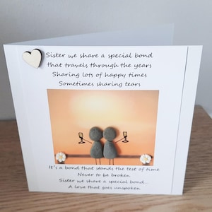 May include: A card with a painted image of two figures made of stones holding glasses of champagne. The card has a poem about sisterhood that reads "Sister we share a special bond that travels through the years. Sharing lots of happy times. Sometimes sharing tears. It's a bond that stands the test of time. Never to be broken. Sister we share a special bond... A love that goes unspoken."