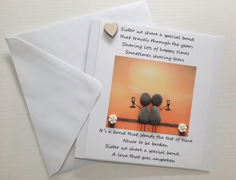 May include: A card with a handwritten message about sisterhood. The card features a sunset background with two figures made of stones holding glasses of wine. The text reads "Sister we share a special bond that travels through the years Sharing lots of happy times Sometimes sharing tears. It's a bond that stands the test of time Never to be broken Sister we share a special bond..... A love that goes unspoken"