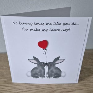 Może przedstawiać: Biała kartka z tekstem "No bunny loves me like you do... You make my heart hop!" i dwoma szarymi kr&oacute;likami z czerwonym balonem w kształcie serca między nimi.