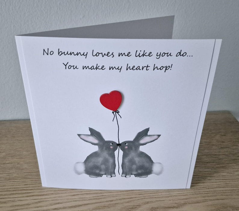 Może przedstawiać: Biała kartka z tekstem "No bunny loves me like you do... You make my heart hop!" i dwoma szarymi kr&oacute;likami z czerwonym balonem w kształcie serca między nimi.