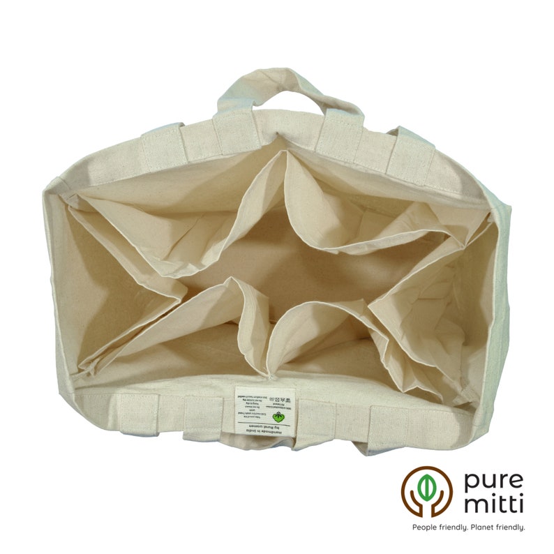 May include: A beige canvas tote bag with six interior pockets. The bag has two handles and a label with the text "pure mitti" and "People friendly. Planet friendly."