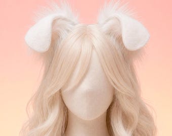 May include: A wig with long, wavy, light blonde hair and white bunny ears. The ears are fluffy and upright, and the wig is styled on a mannequin head. The background is a gradient of pink and peach.