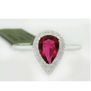 Puede incluir: Un anillo de plata con una piedra roja en forma de pera rodeada de un halo de pequeñas piedras blancas.