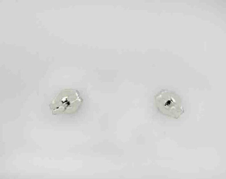 Op de afbeelding: Een paar kleine, zilveren oorbelletjes. De oorbelletjes zijn rond en hebben een licht getextureerd oppervlak.