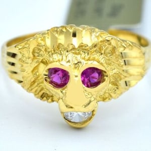 May include: A gold ring with a lion's head design. The lion has pink ruby eyes and a single diamond in its mouth.