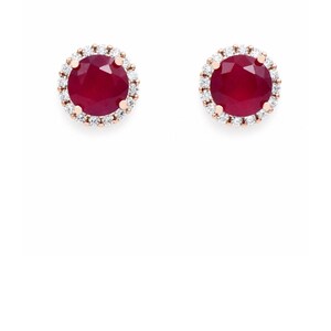 May include: A pair of round stud earrings featuring a deep red circular gemstone at the center of each piece. Each central stone is surrounded by a halo of small, clear, sparkling white stones set in a metallic frame, creating a classic design.