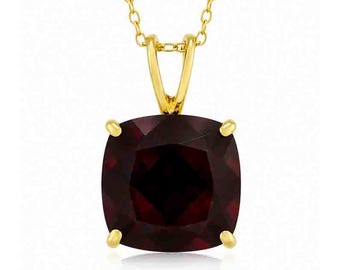 May include: A gold-colored pendant necklace featuring a cushion-cut, deep red gemstone. The gemstone is held in place by four gold prongs, and the chain is also gold.