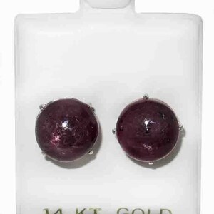Könnte beinhalten: Ein Paar Rubinohrringe, gefasst in 14 Karat Gold. Die Ohrringe sind rund und haben eine tiefrote Farbe. Die Ohrringe werden in einer durchsichtigen Plastikbox mit weißem Hintergrund präsentiert.