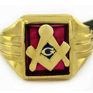 May include: A gold ring with a red stone featuring a gold Masonic symbol with a blue eye and the letter G.