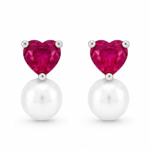 May include: A pair of stud earrings. Each earring has a heart-shaped, ruby-red gemstone above a white pearl. The earrings are set in silver-coloured metal and are shown against a white backdrop.