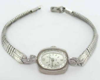 May include: A silver Bulova wristwatch with a rectangular face and a silver metal band. The watch face has black Roman numeral hour markers and black hands.