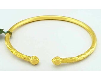 May include: A gold-colored open cuff bracelet. The bracelet has a smooth, rounded band that widens at the ends, terminating in decorative, rounded finials. The bracelet is likely made of metal and is displayed against a white background.