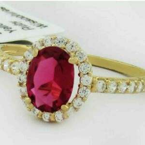Peut inclure: Une bague en or avec un grand rubis ovale entouré d'un halo de petits diamants. La bague a une bande de petits diamants.