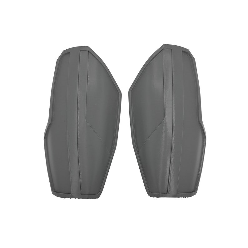 Pu&ograve; includere: Due pezzi di armatura protettiva grigi e curvi. Ogni pezzo ha una forma sagomata con linee verticali e angolate, che suggeriscono un design aderente. I pezzi sono realizzati in un materiale solido e opaco.