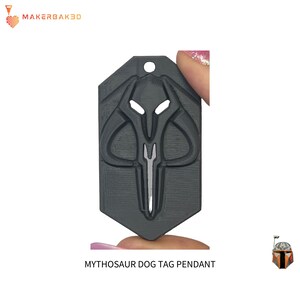May include: A dark gray Mythosaur dog tag pendant. The pendant features a detailed design of the Mythosaur skull symbol with a hole at the top for attachment. The text "MYTHOSAUR DOG TAG PENDANT" is at the bottom.